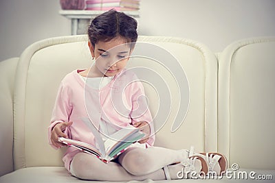 Cute hispanic little girl reading book on couch Stock Photo