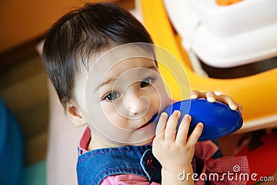 Cute infant child baby girl toddler sitting and eating blue toy Stock Photo