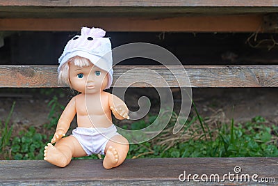 Cute kewpie doll sits on wooden bench in country house yard Stock Photo