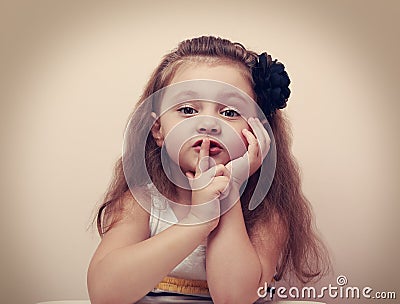 Cute kid girl showing silence sign the finger near lips. Vintage Stock Photo