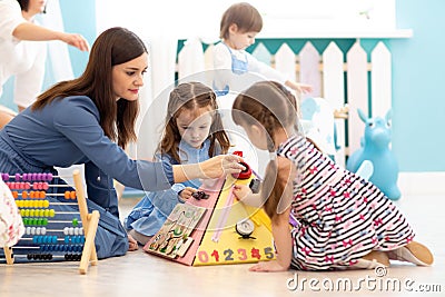 Cute kids playing with busy board in kindergarten. Children`s educational toys. Wooden game board. Stock Photo