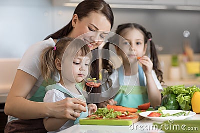 Cute kids tasting vegetables as they prepare a meal with their mother in the kitchen Stock Photo