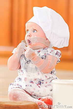 Cute liitle girl in chef`s hat sitting on the kitchen floor soil Stock Photo