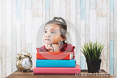 Cute little asian girl gazing and looking at empty space against books on table Stock Photo