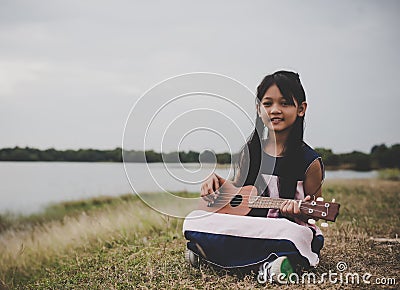 Cute little asian girl sitting on grass and play ukulele in park Stock Photo