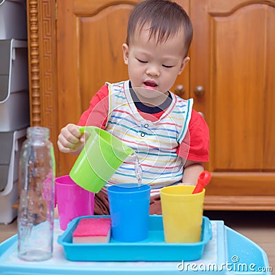 Asian 18 months old toddler boy child having fun pouring water into cup, Wet Pouring Montessori Preschool Practical Life Activitie Stock Photo