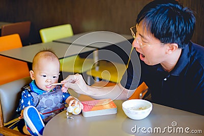 Cute little Asian toddler baby boy child doesn`t want to eat food, Dad feeding kid with spoon in high chair Stock Photo