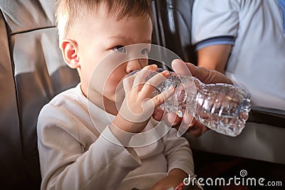 Cute little Asian 3 years old toddler boy child drinking water from bottle during flight on airplane. Little kid feeling earache Stock Photo