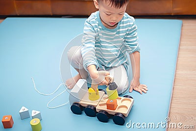 Asian 3 - 4 years old toddler boy child having fun playing with wooden building blocks and loader car toys indoor at nursery / Stock Photo