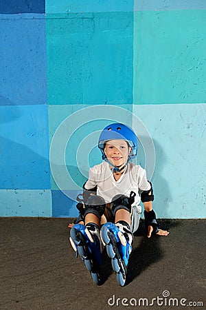 Cute little athletic boy on roller sitting against the blue graffiti wall Stock Photo