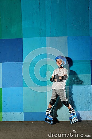 Cute little athletic boy on roller standing against the blue graffiti wall Stock Photo
