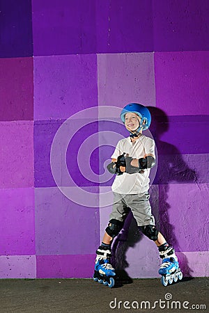 Cute little athletic boy on roller standing against the purple graffiti wall Stock Photo