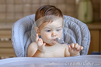 Cute little baby boy looking at spoon in his hand with funny bewildered face expression Stock Photo