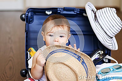 Cute little baby boy inside packed suitcase with straw hat in his hands Stock Photo