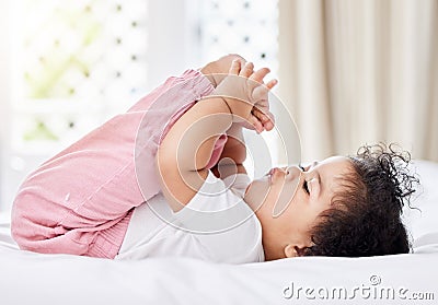 Cute little baby girl playing with her feet,lying on the bed in her bedroom. Small hispanic baby holding and looking at Stock Photo