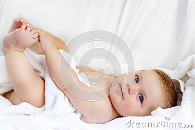 Cute little baby playing with own feet after taking bath. Adorable beautiful girl wrapped in white towels Stock Photo