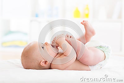 Cute little baby weared diaper playing with his legs and sucking on his foot Stock Photo