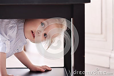 Cute little blond girl in striped shirt climbed in recess table Stock Photo