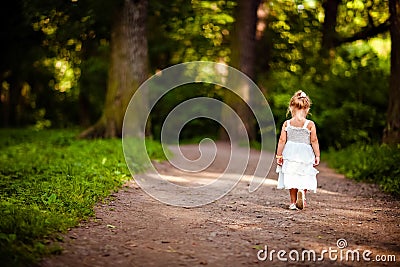 Cute little blonde girl in a white dress walking down the path i Stock Photo