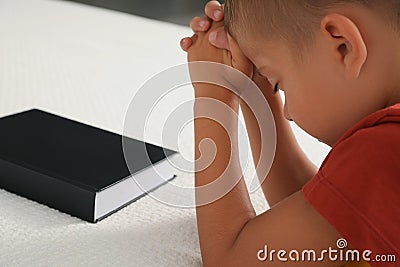 Cute little boy with hands clasped together saying bedtime prayer over Bible at home, closeup Stock Photo