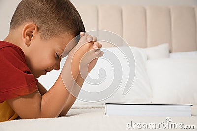 Cute little boy with hands clasped together saying bedtime prayer over Bible at home. Space for text Stock Photo