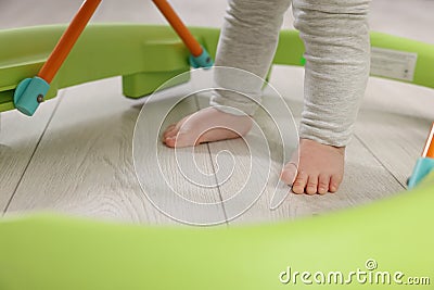 Cute little boy making first steps with baby walker on wooden floor, closeup Stock Photo