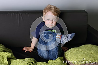 Cute little boy sits and thinks on black couch Stock Photo