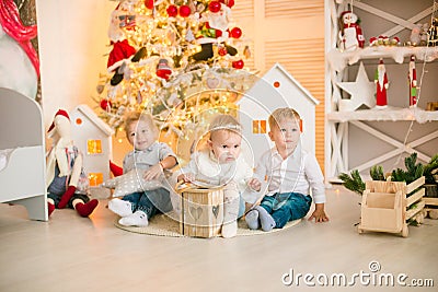 Cute little boys with blond hair plays with little girl in a bright room decorated with Christmas garlands Stock Photo