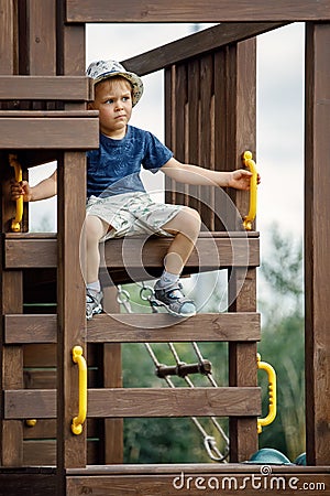 A cute little brave boy sitting at the top of the wooden playground Stock Photo