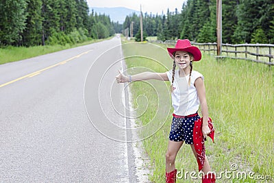 Cute little cowgirl trying to hitch hike a ride on a lonely road Stock Photo