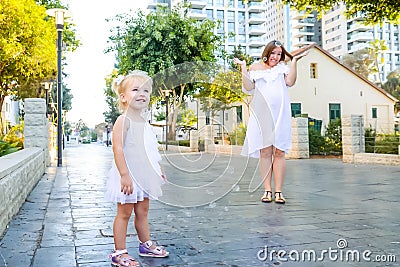 Cute little emotional blondy toddler girl in dress with pregnant mother playing, catching soap bubbles during walk in the city par Stock Photo