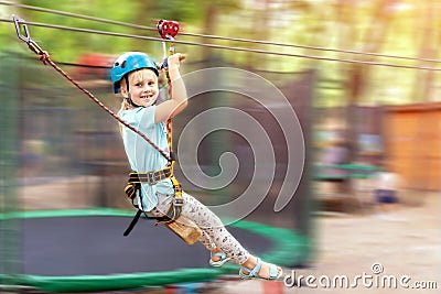 Cute little funny caucasion blond girl in helmet having fun riding rope zipline in adventure park. Children outdoor extreme sport Stock Photo
