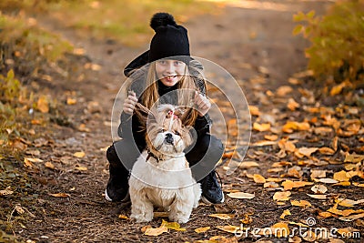 Cute little girl in a black coat with a dog walk in the park. A child is training a dog. Faithful friends of man. Leisure with Stock Photo