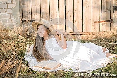 Cute little girl with blond long hair in a summer field at sunset with a white dress with a straw hat Stock Photo