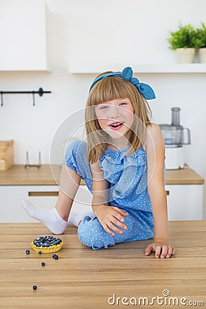 Cute little girl in blue dress sits on a table and and smiles Stock Photo