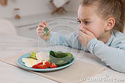 Cute little girl covering mouth and refusing to eat dinner in kitchen Stock Photo