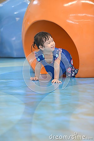 Cute little girl crawling on floor through tunnel in gym class Stock Photo