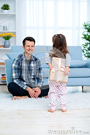 Cute little girl, daughter, sister gives a gift box to young dad father or brother. Both are smiling. Father`s day holiday concep Stock Photo