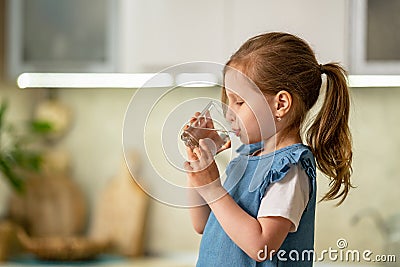 Cute little girl drinking water in kitchen at home. Water balance Stock Photo