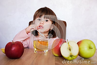 Cute little girl drinks apple juice using drinking straw. Baby girl with juice and fruit apples Stock Photo