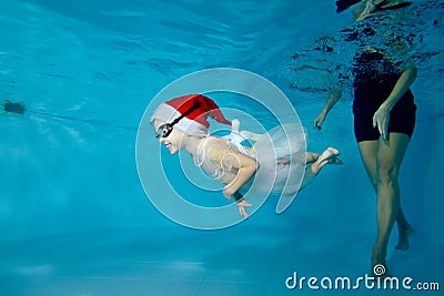 Cute little girl is engaged in scuba diving in a children`s pool with a trainer. She swims under the water in a Santa Stock Photo