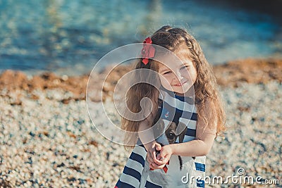 Cute little girl enjoying summer time on sea side beach happy playing with red star and tiny toy anchor on sand wearing nobby clot Stock Photo