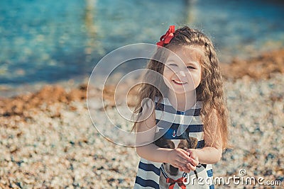 Cute little girl enjoying summer time on sea side beach happy playing with red star and tiny toy anchor on sand wearing nobby clot Stock Photo