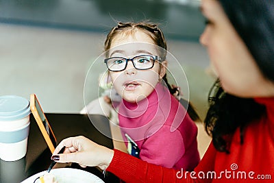 Cute little girl in eyeglasses using smartphone indoor in lobby or coffee shop. Children and gadgets concept. Stock Photo