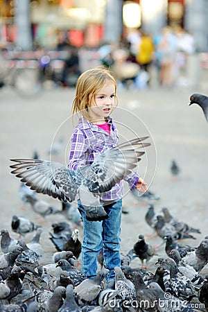 Cute little girl feeding and chasing birds on Dam Square in Amsterdam on summer day Stock Photo