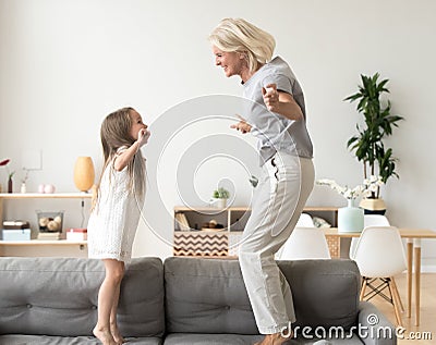 Cute little girl playing with grandmother jumping on couch toget Stock Photo