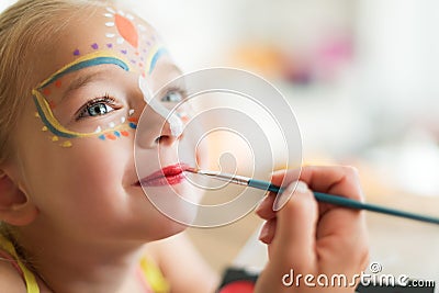 Cute little girl having her face painted for Halloween party. Halloween or carnival family lifestyle background. Face painting. Stock Photo