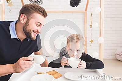 Cute little girl and her father drink tea with cookies at home. Stock Photo