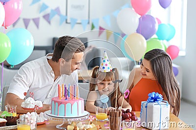 Cute little girl and her parents celebrating birthday at table with cake Stock Photo