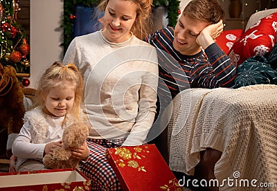 Cute little girl with her young parents celebrating Christmas at home by the fireplace Stock Photo